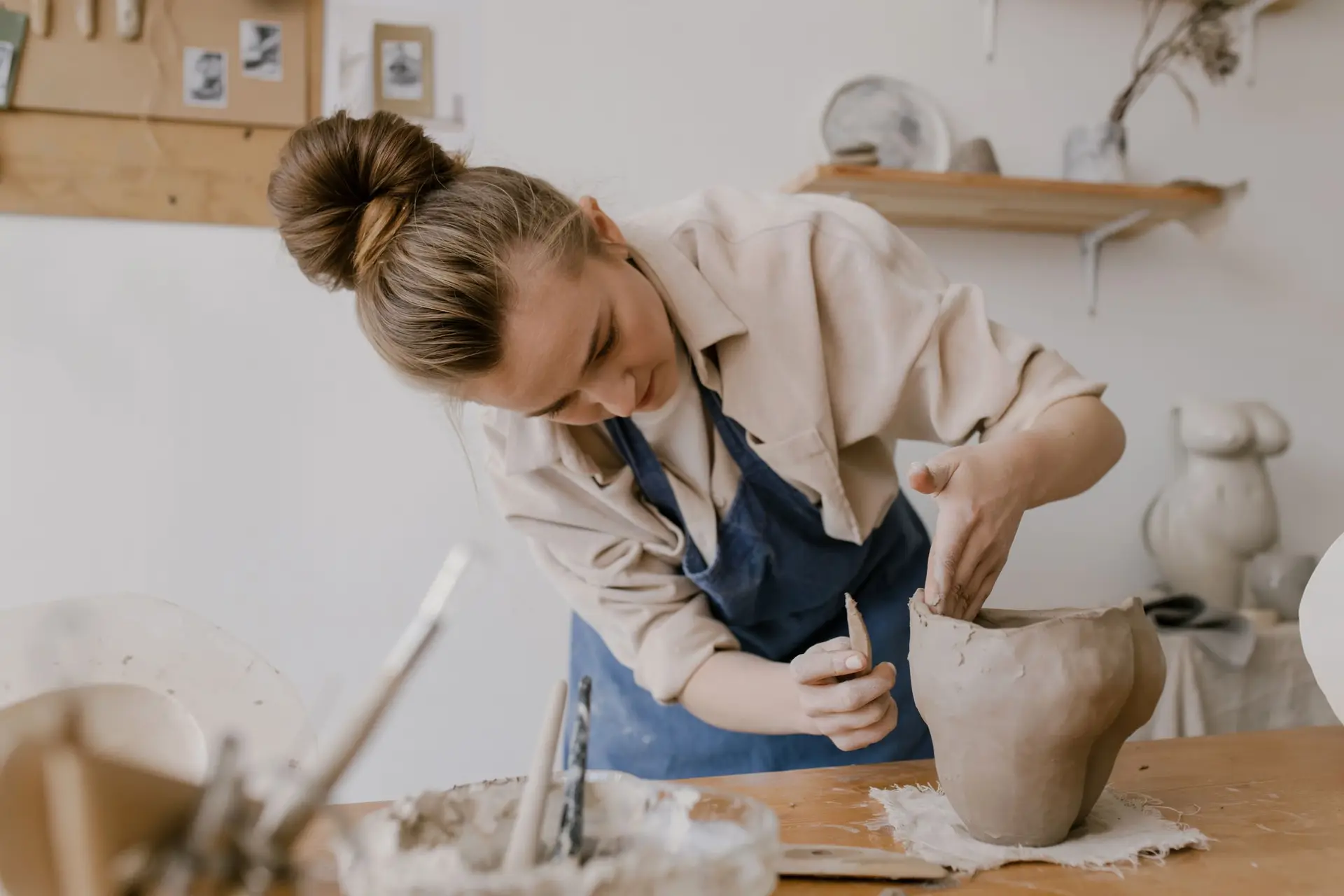 A potter shaping a clay vessel at her workbench